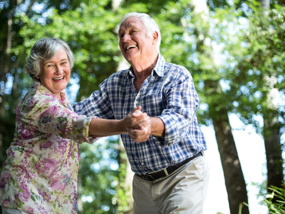 senior man and woman, in a floral top, dancing together and laughing