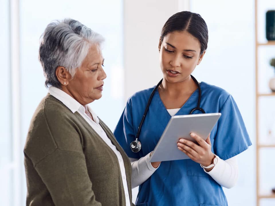female healthcare worker holding an ipad and pointing, talking to a senior woman