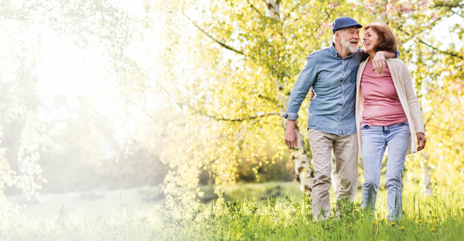 older couple walking through a field of blooming trees and grasses, with their arms around each other