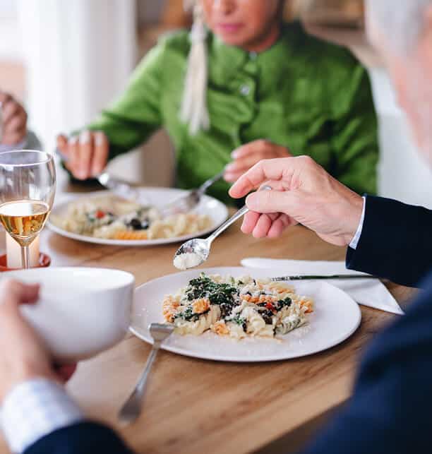 woman in green blouse eating next to a man in a blue sport coat eating pasta with parmesan cheese