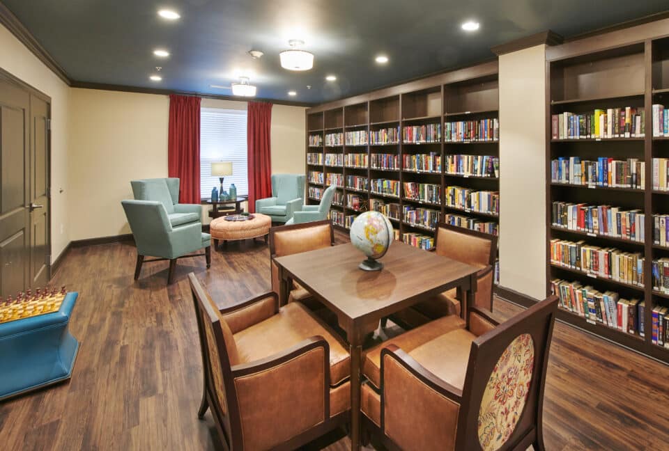 library with chess game, two tables with chairs, globe and books on shelves