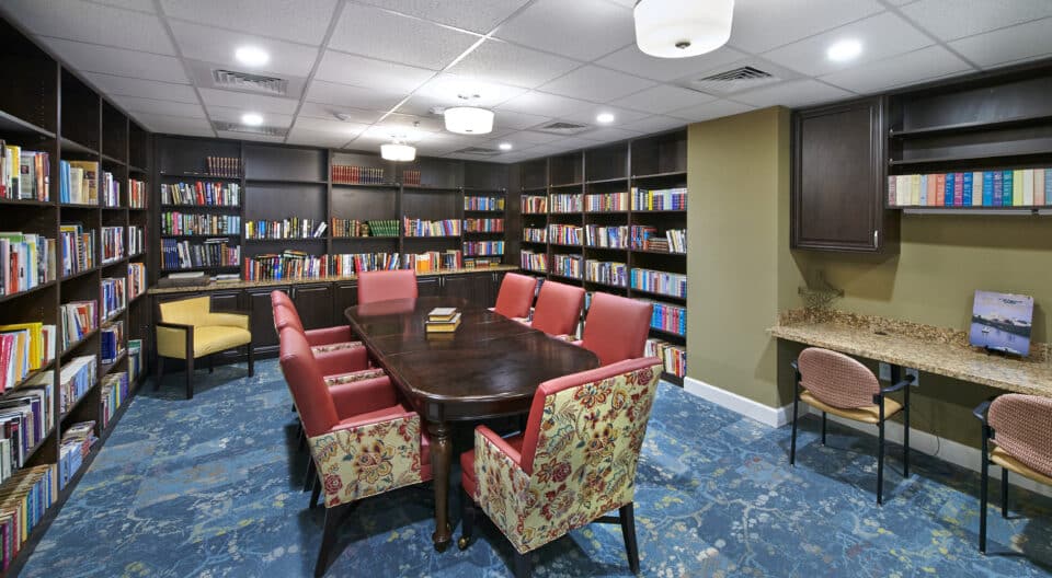 long table with upholstered chairs, book shelves with books, computer station