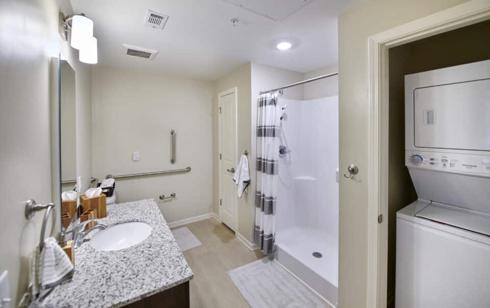 bathroom with white stackable washer/dryer, walk in shower, sink vanity